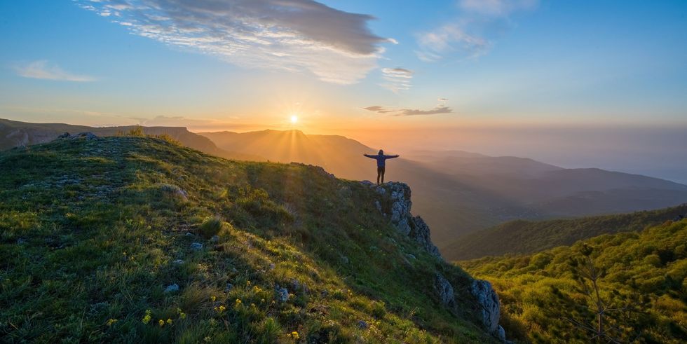 A person standing on top of a hill with arms outstretched.