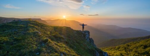 A person standing on top of a hill with arms outstretched.