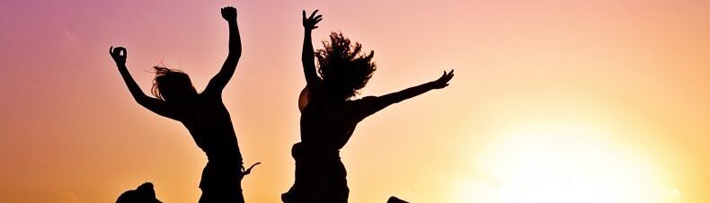 Two people jumping in the air at sunset.